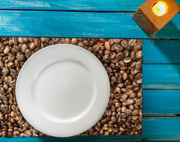 浅蓝色的桌子上有单独装饰的咖啡豆和一个白色的盘子，可以在烛光下使用。图片下载