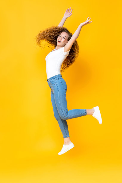 漂亮的女人跳跃自由与双手隔离在黄色背景图片下载