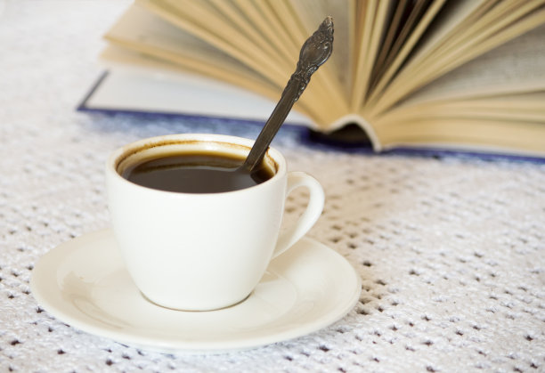 白色的桌子背景上放着咖啡杯和茶托，还有一本打开的书图片下载