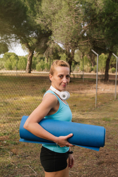 一个运动女性在瑜伽或普拉提课后与她的垫子和运动设备走在街上的垂直照片。生活方式与健身理念图片下载