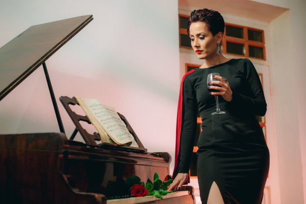有魅力的女人触摸着钢琴键盘，拿着酒杯图片下载