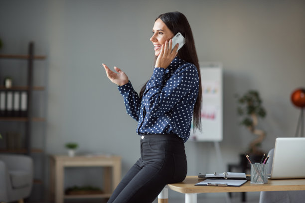 迷人的年轻女子的侧面照片坐在桌子上谈论智能手机客户端室内工作在办公室工作站图片下载