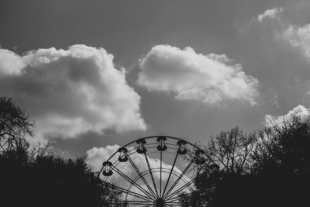 一个扇形的摩天轮在公园的阴凉处，它的上方是淡淡的多云的天空。黑白大气照片旋转公园图片下载