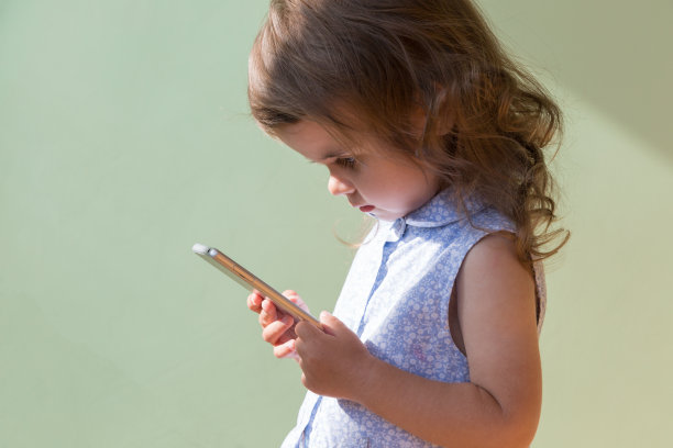 美丽的蹒跚学步的女孩玩智能手机。图片下载