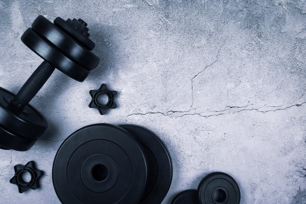 顶视图的黑色哑铃和不同的重量板上灰色纹理的背景。平的。图片下载