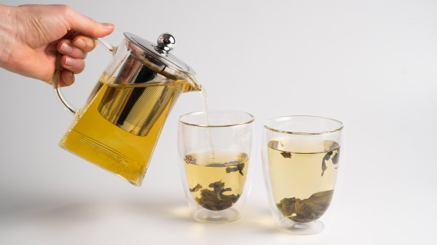 用手将白茶从透明茶壶中倒入玻璃杯中。白底蒸白茶图片下载