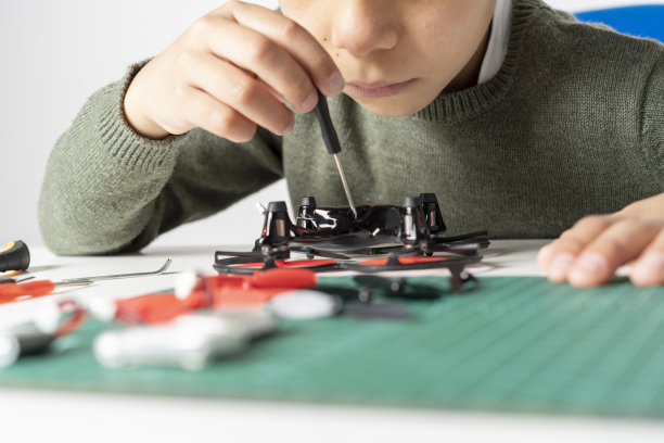 集中的男孩修理他的玩具无人机与一个工具在他的手和他的无人机的各种备件的近距离。有选择性的重点图片下载
