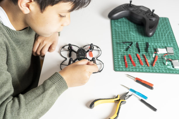 集中的男孩修理他的玩具无人机在他的手螺丝刀和各种工具和备件在桌子上他的无人机。图片下载