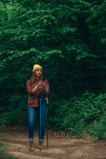 一名徒步女在森林里用登山杖和智能手机行走图片下载