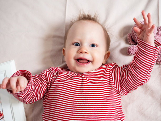 一个女婴的肖像，8个月大，玩一个软玩具，俯视图，特写。一个淘气、漂亮的女孩，有着白皙的皮肤和头发，蓝色的大眼睛。真实的孩子的情感，笑声图片下载