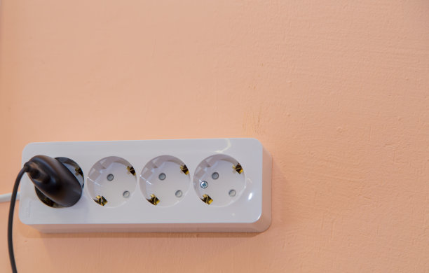米色墙壁上插着一个黑色插头的插座。图片下载