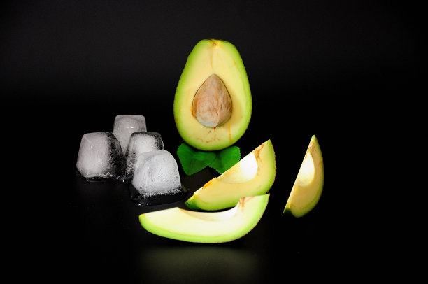将熟透的鳄梨切成片和融化的冰块，在黑色的背景上。图片下载