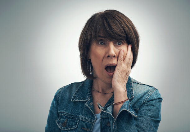 一个在灰色背景下看起来很震惊的妇女的摄影图片下载