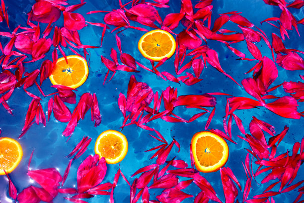 红色的花瓣和橙色的薄片漂浮在蓝色的水面上图片下载