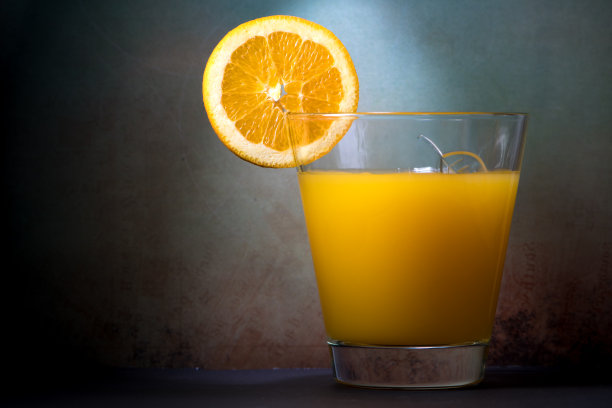 一杯橙汁，配上一片橘色水果，背景是忧郁的橘色蓝色。酒精在岩石玻璃。图片下载