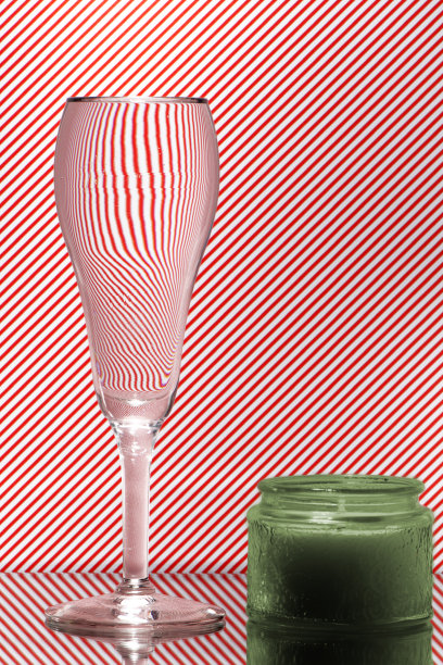 在红色和白色条纹背景上的郁金香香槟杯折射的光。蜡烛的抽象玻璃艺术图片下载