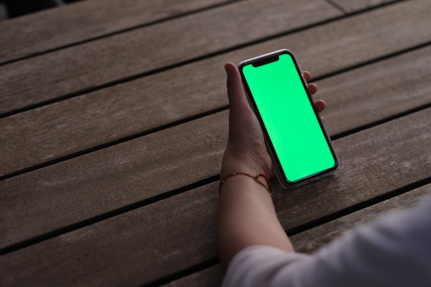 晚上在木桌上手持绿色屏幕的手机图片下载