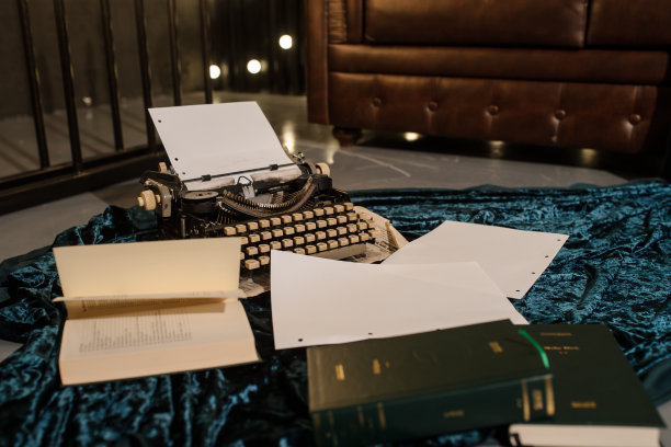 一张打字机在一张报纸上的照片，地板上有深蓝色的天鹅绒织物，里面有纸，旁边是一个棕色的皮沙发图片下载