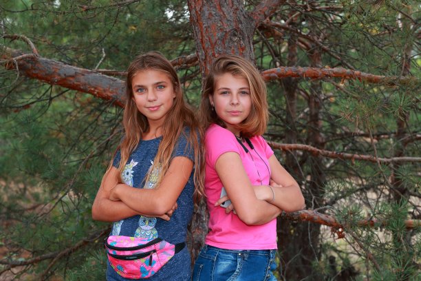 两个十几岁的女孩在森林的松树附近摆姿势的肖像。真实的人图片下载