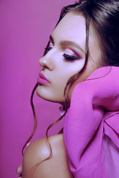 美丽的时尚女孩长卷发摆造型与一个粉红色的蝴蝶结。画室里以粉红色为背景的女孩。时尚、美丽。明亮的化妆。头发化妆品，健康头发。图片下载