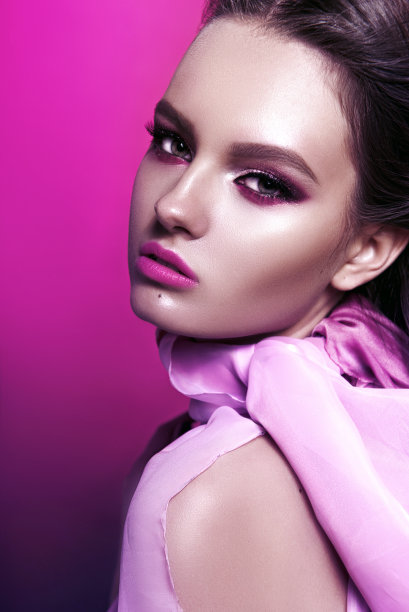 美丽时尚的女孩长发卷发摆着粉红色的蝴蝶结。画室里粉红色背景的女孩。时尚、美丽。明亮的化妆。头发化妆品，健康的头发。图片下载