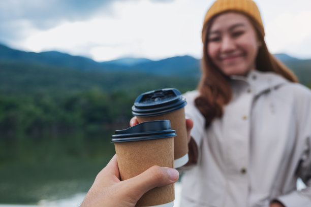 一对情侣在山和湖的旅行中手握咖啡杯，互相碰杯图片下载
