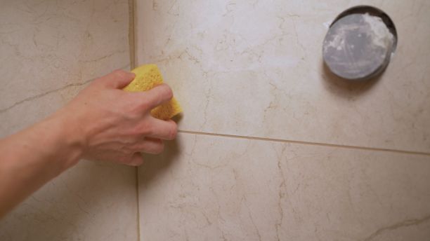 一个工人用海绵清洗浴室的瓷砖。一个戴着黄色防护手套的男人在浴室里清洗一块脏兮兮的瓷砖。图片下载