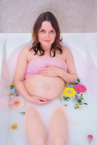 一个孕妇用手抱着她的肚子在一个有水的浴缸里图片下载