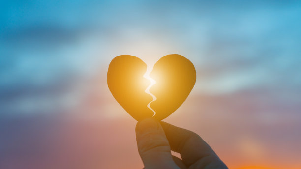 夕阳下，一只手抱着一颗破碎的心。图片下载