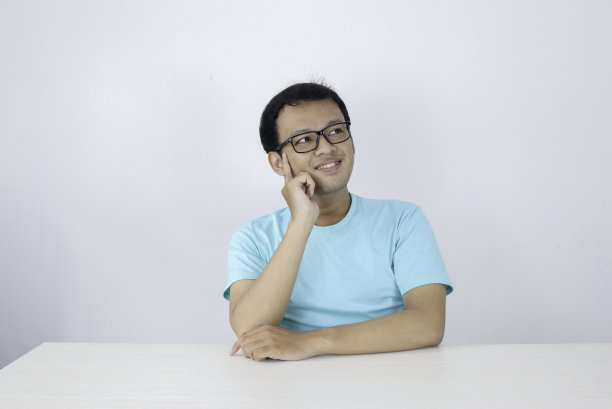 年轻的亚洲男子穿着蓝色的衬衫和眼镜与思考和看的想法手势在上面的空白空间图片下载