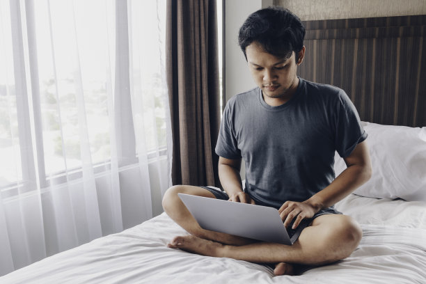 一个严肃的亚洲人正在床上用笔记本电脑工作。自由职业者成功的生活理念。图片下载