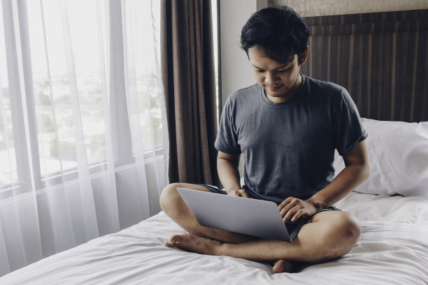 一个严肃的亚洲人正在床上用笔记本电脑工作。自由职业者成功的生活理念。图片下载