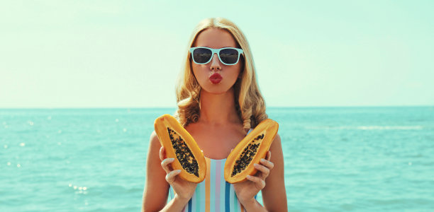 夏天的年轻女子在沙滩上的肖像木瓜吹她的嘴唇发送亲吻在一个海洋的背景图片下载