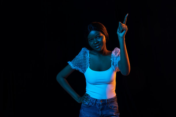 一个年轻的非洲美丽的女孩孤立在混合霓虹灯的黑暗背景。图片下载