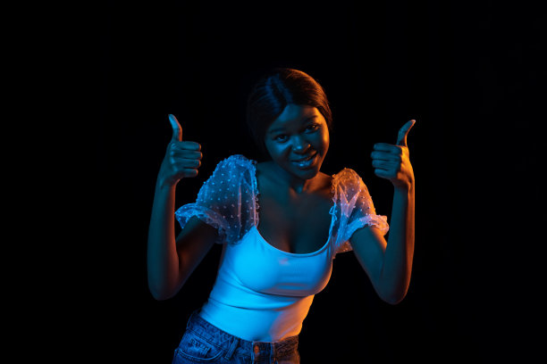 一个年轻的非洲美丽的女孩孤立在混合霓虹灯的黑暗背景。图片下载