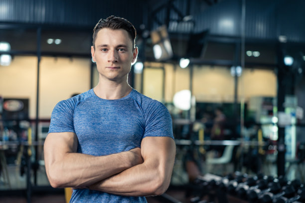 积极的白种人健身运动教练锻炼保持肌肉和二头肌的健康。健美运动员男性双臂交叉微笑地站在体育场或健身俱乐部的镜头前图片下载