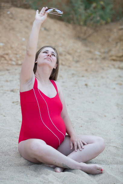 身着红色连体泳衣的孕妇在沙滩上休息图片下载