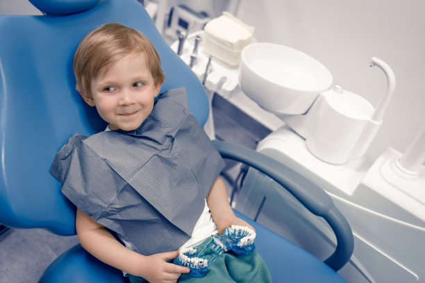 一个孩子坐在牙科医生的牙科椅上。快乐狡猾的白种人学龄前儿童治疗牙齿，快乐。图片下载