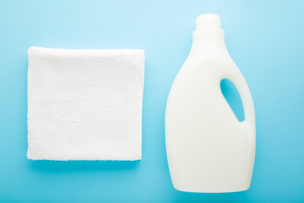 白色的毛巾和塑料瓶在浅蓝色的桌子背景。柔和的颜色。特写镜头。洗衣服的洗涤剂。自顶向下的观点。图片下载