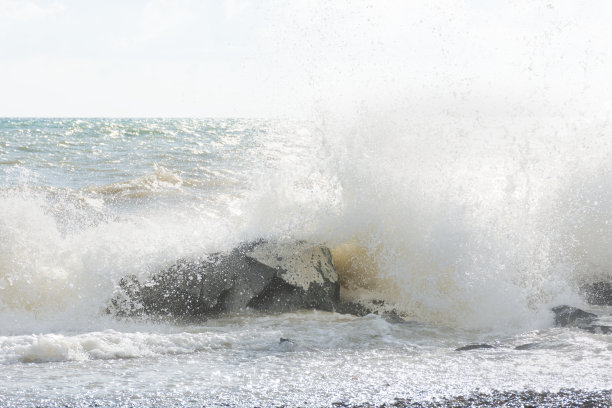 明亮的阳光下，海浪在海滩上翻滚。美丽的淡灰色海背景。图片下载