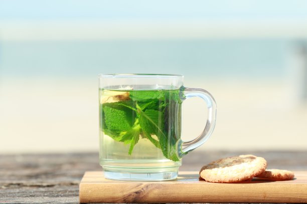 薄荷茶，绿叶和饼干在海滩前图片下载