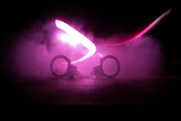 警方夜间突袭，你将被逮捕。手铐的轮廓和警车在后面。在雾蒙蒙的背景下，红色和蓝色警灯闪烁。图片下载