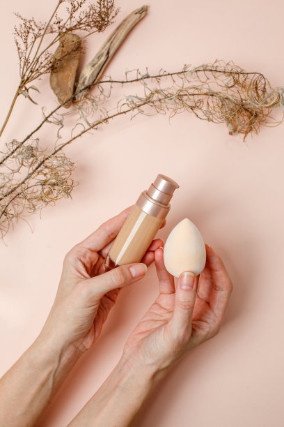 粉底用时尚的米褐色泥土色调背景，由女性亲手打上粉底。专业化妆用的BB霜。化妆女性配件，液体流体，时尚图片下载