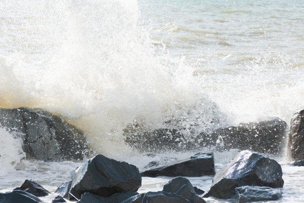 明亮的阳光下，海浪在海滩上翻滚。美丽的淡灰色海背景。图片下载