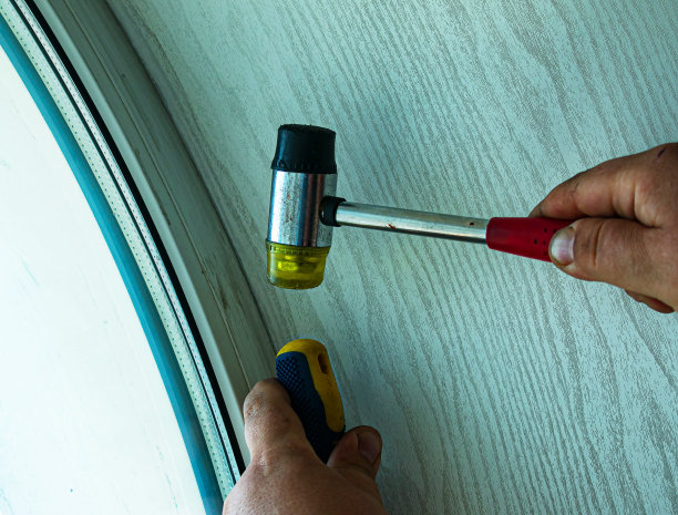 一个人用螺丝刀和特制的木槌把塑料窗户或门弄直。男性的手靠近。图片下载