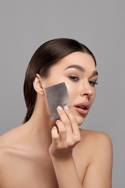 皮肤护理。年轻女子用吸油纸去脸上的油。照片美丽的女人与光滑和健康的皮肤。美丽的概念图片下载