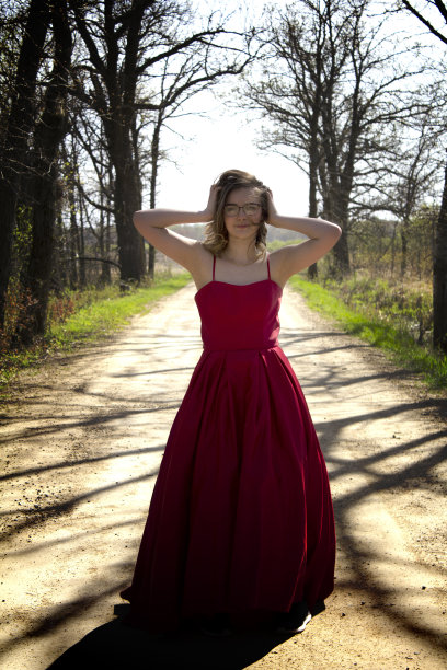 年轻的女人在红裙子站在一个老土路与手在头发微笑全长相机图片下载