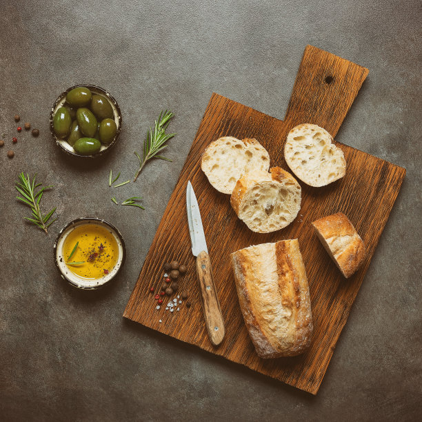 新鲜的脆皮意大利面包切片，橄榄油，橄榄和迷迭香，在深色的垃圾背景。传统的意大利美食。前视图。广场的照片图片下载