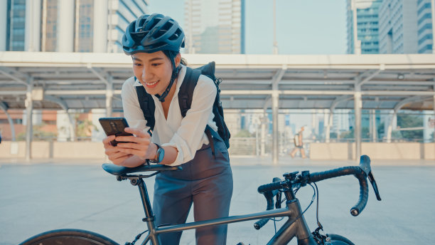 微笑亚洲女商人背包用智能手机看相机在城市站在街道上骑自行车上班在办公室。图片下载