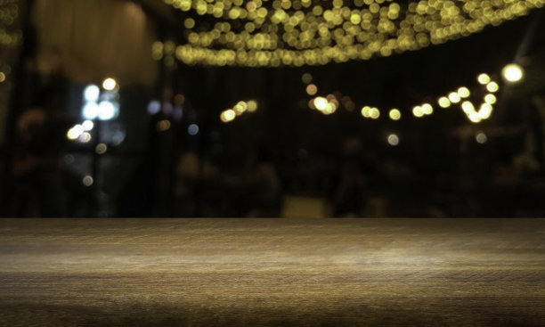 吧台吧台的空木桌顶与抽象模糊的灯光散景在黑暗的夜晚酒吧，餐厅，咖啡馆的背景。生活方式派对和庆祝概念。桌面展示产品的空白空间。图片下载